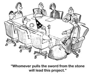 Teamwork b&w cartoon showing a team meeting and a big stone with a sword in it.  The male team leader says 'whomever pulls the sword from the stone will lead this project'.