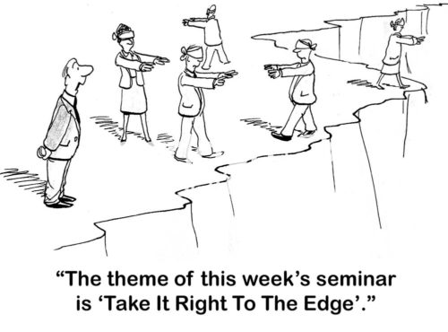 Teamwork b&w cartoon of five blindfolded businesspeople walking along a cliff edge. The boss shouts out, 'the theme of this week's seminar is "take it right to the edge"'.