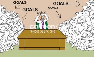 Office color cartoon showing a stressed businessman sitting at his desk gritting his teeth and pulling at his hair with both hands. There are stacks and stacks of GOALS on both sides of his desk.