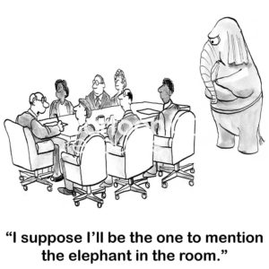 B&W office cartoon showing 7 people at a meeting table and a large elephant standing on its hind legs at the end of the table. The male meeting leader states, 'I suppose I'll be the one to mention the elephant in the room'.